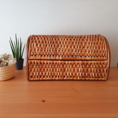 a wicker box sitting on top of a wooden table next to a potted plant