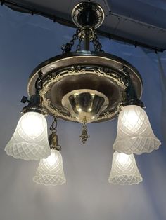 a chandelier with five lights hanging from it's ceiling and some glass shades on the light fixture