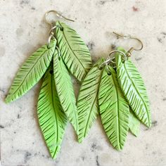 three green leaf shaped earrings sitting on top of a marble counter