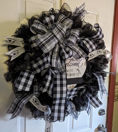 a black and white wreath hanging on the front door with welcome signs attached to it