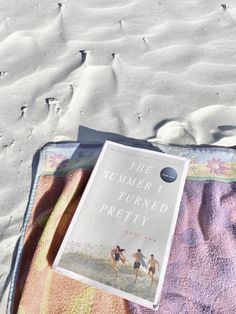 a book sitting on top of a blanket next to a pink and yellow towel in the sand