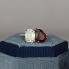 a red and white diamond ring sitting on top of a blue velvet cushioned box