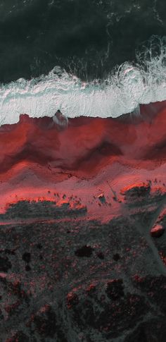 an aerial view of the ocean with red and white waves coming in from the water