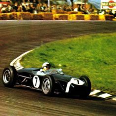 a man driving a race car on a track with people watching from the sidelines