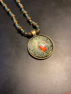 a necklace with a red bead hanging from it's side on a table