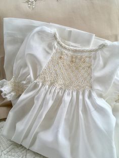 Hand Smocked Baby Day Gown to suit Newborn to 6 months approx. (depends on child) Made in a fine Ivory/Off White 100% Cotton Voile fabric with buttons down the back to close. Hand smocked and embroidered at the front between the raglan sleeves in ivory and ecru, with a bound neckline hand embroidered with featherstitching and smocked sleeves with fine cotton lace trim. Raglan sleeves allow for a longer wear time and are smocked and edged with fine cotton lace trim. Daygown measures 55cm (21 1/2" Elegant Fitted Smocked Dress With Lace Trim, Elegant Smocked Dress With Smocked Cuffs For Baptism, White Lace Trim Smocked Dress For Daywear, White Smocked Dress With Lace Trim For Daywear, Elegant White Smocked Dress With Lace Trim, Elegant Smocked Ruffle Dress For Baptism, White Baptism Dress With Smocked Bodice For First Communion, White Fitted Smocked Dress For Baptism, Elegant Baptism Dress With Smocked Bodice