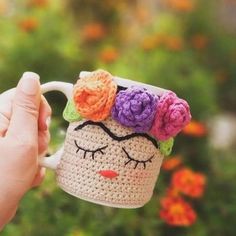 a hand holding a crocheted coffee cup with flowers on it's head