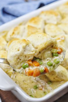 a spoon full of chicken pot pie with peas and carrots on top, in a white casserole dish