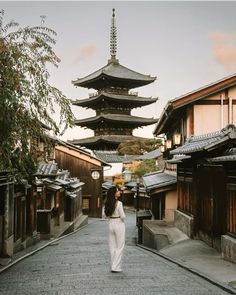 a woman is walking down the street in front of some buildings and tall pagodas