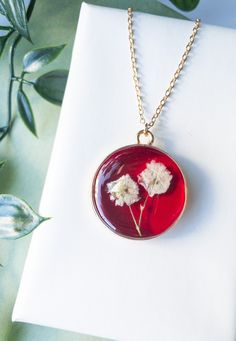 two white flowers in a red glass pendant on a gold plated chain with green leaves