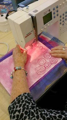 an older woman is using a sewing machine to sew on some fabric with her hands