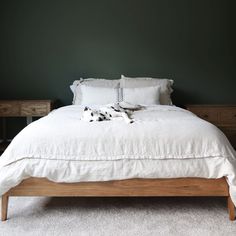 a bed with white linens and pillows in a green walled room, next to two nightstands