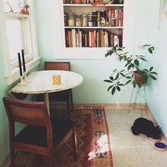 a cat laying on the floor next to a table and bookshelf in a room