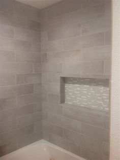 a bath tub sitting under a window next to a white tiled shower wall in a bathroom