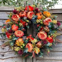 a wreath with orange flowers and greenery hanging on a wooden fence post in front of a wood paneled wall