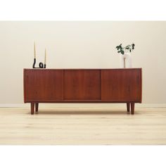 a wooden sideboard with two vases on top and one potted plant in the middle