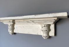 an old white painted shelf with two wooden brackets on the top and bottom, against a gray wall