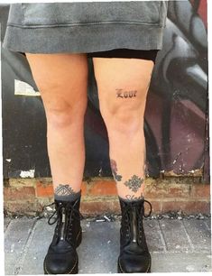 the legs and ankles of a woman with tattoos on her leg, standing in front of a graffiti covered wall