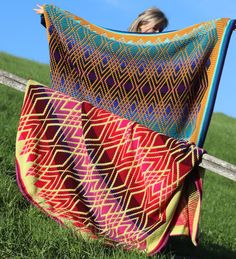 a woman holding up a colorful blanket in the grass