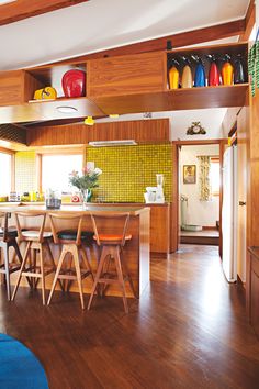 a kitchen with wooden flooring and open shelving above the bar area has colorful vases on shelves