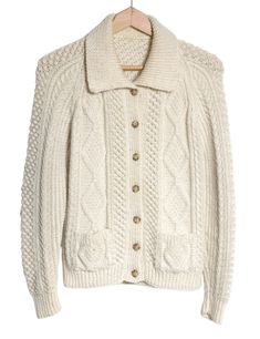 a white cable knit jacket hanging on a wooden hanger