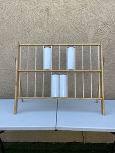 three white candles sitting on top of a wooden rack next to a wall and grass