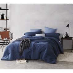 a bed with blue comforters and pillows in a white room next to a book shelf