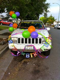 a white car with balloons and streamers on it's hood is parked in the street