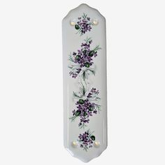 a white plate with purple flowers and pearls on the edge, hanging from a wall