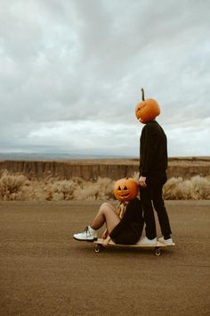 two people with pumpkins on their heads sitting on a skateboard in the desert