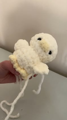 a hand holding a small stuffed animal made out of white yarn with black eyes and tail