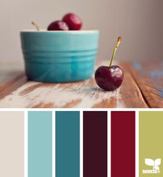 a bowl with two cherries in it on top of a wooden table next to color swatches