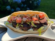 a sandwich with meat, tomatoes and onions on it sitting on top of a white plate