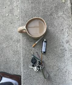 a cup of coffee and some keys are on the ground next to someone's feet