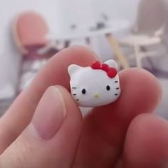 a hand holding a hello kitty ring with a red bow on it's head