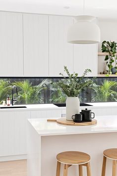 a kitchen with two stools next to a counter top and potted plants on the window sill