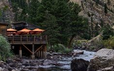 an outdoor dining area with tables and umbrellas on the deck next to a river