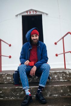 a man with a beard sitting on steps holding a red cup and wearing a blue jacket