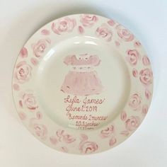 a pink and white plate with a baby's birth date on it, surrounded by roses