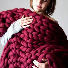 a woman wrapped in a large chunky blanket with her hands on the top of it