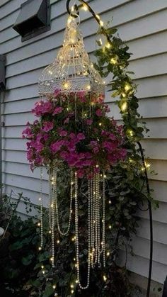 a birdcage with lights hanging from it's sides and flowers in the bottom