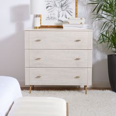 a white dresser sitting in a bedroom next to a plant on top of a rug