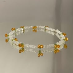 the bracelet is made with glass beads and yellow flowers on white string, sitting on a table