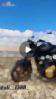 a black motorcycle with gold and silver wheels on the ground in front of a blue sky