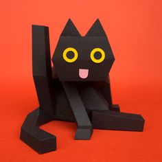 an origami black cat sitting on top of a red surface with yellow eyes