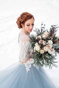 a woman in a blue and white dress holding a bridal bouquet with greenery