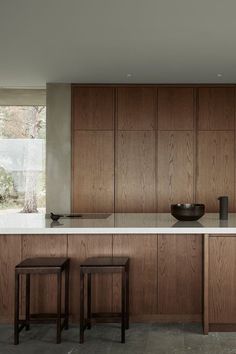 a modern kitchen with wooden cabinets and white counter tops, along with two stools