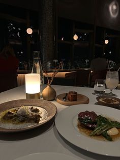 two white plates with food on them sitting on a table in a dimly lit room