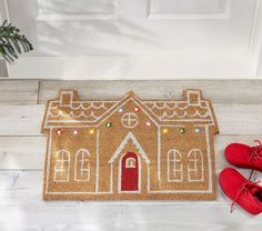 a door mat with a gingerbread house on it and red shoes next to it