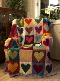 a crocheted blanket with hearts on it sitting on a chair in front of a window